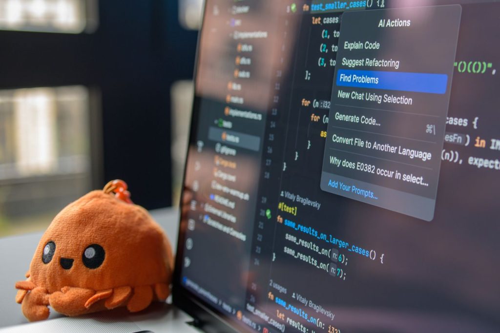 pexels photo 34804015 A laptop screen showing a code editor with a cute orange crab plush toy beside it.